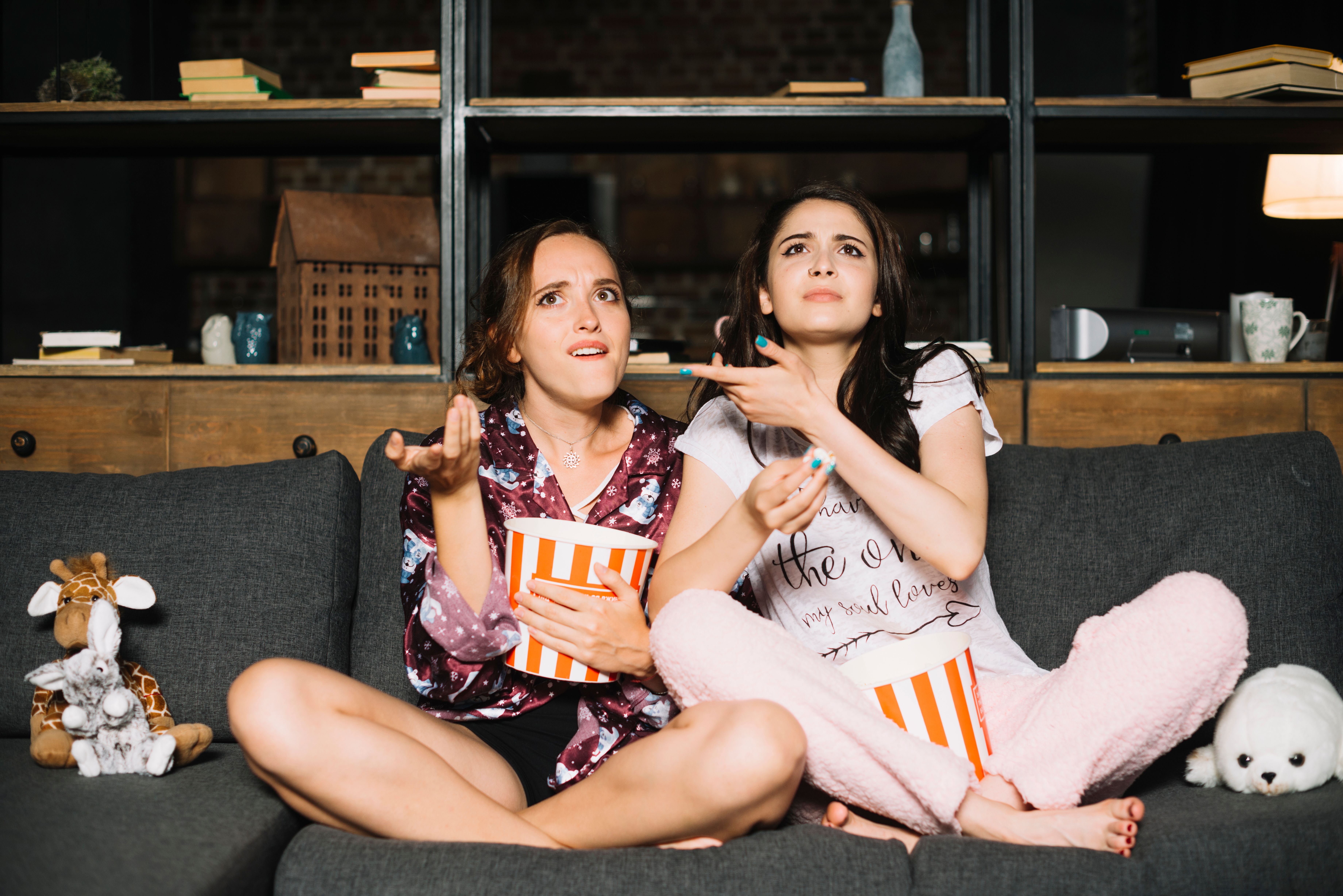 two-female-friends-watching-television-shrugging.jpg